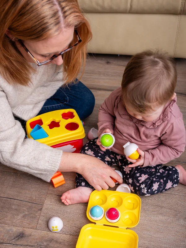 Louise Cook sitting on the floor playing with her baby and colourful shape-sorting toys