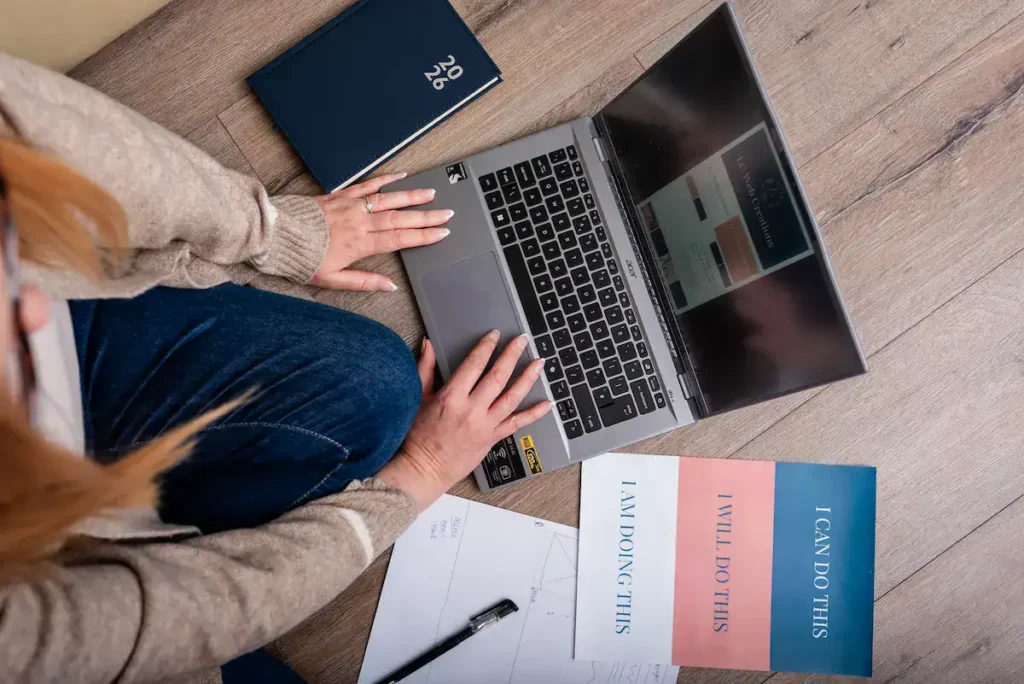 Overhead view of Louise Cook, Galway web designer, working on a laptop on the floor surrounded by wireframe sketches, a diary, and motivational cards