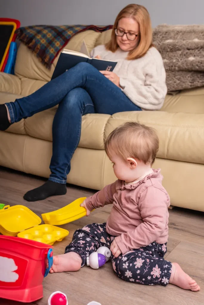 Louise Cook, Galway web designer, reading and taking notes on the sofa while her baby plays independently on the floor nearby