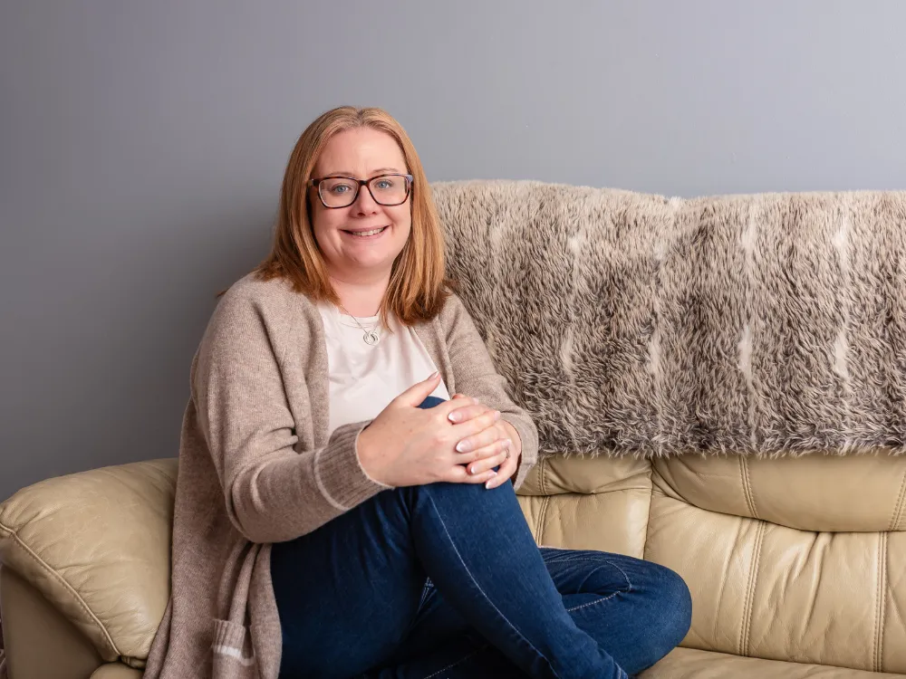 Louise Cook, Galway web designer, sitting on the corner of a sofa with a warm smile