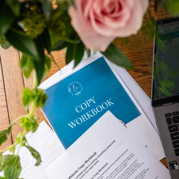 The LC Web Creations Copy Workbook on a wooden table with some flowers