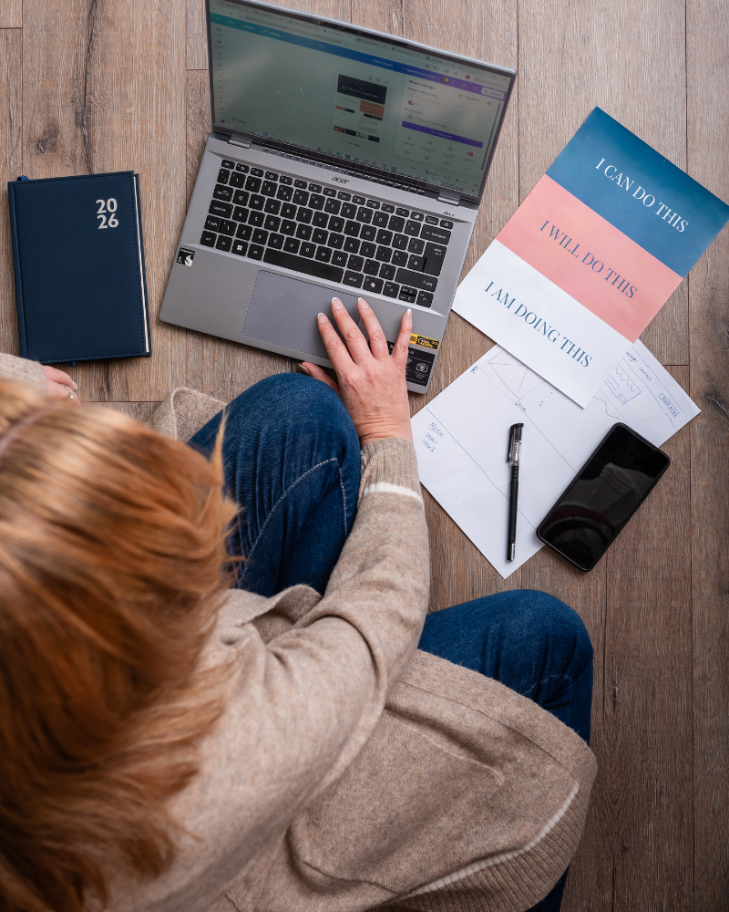 Overhead view of Louise Cook, Galway web designer, working on a laptop on the floor surrounded by wireframe sketches, a diary, and motivational cards