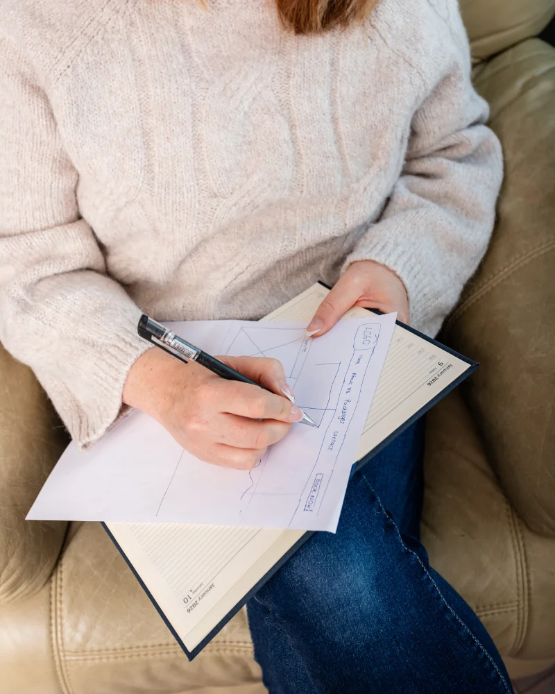 Louise Cook, Galway web designer, sitting on the couch and drawing out the wireframe for a website.