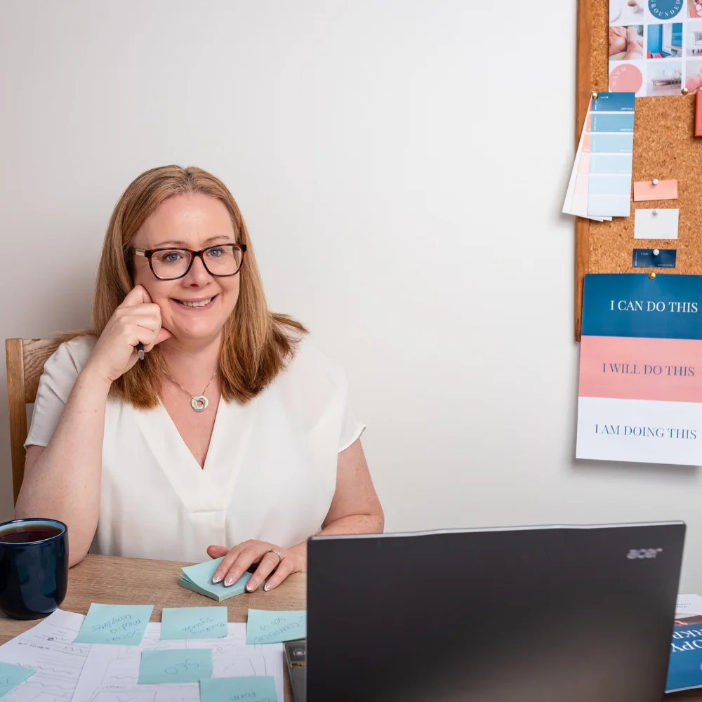 Louise Cook, Galway web designer, smiling at her desk with a laptop, sticky notes, and a cork inspiration board.