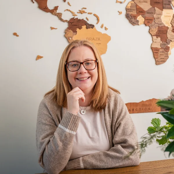 Galway web designer sitting at desk smiling, ready to launch new website with world map in background